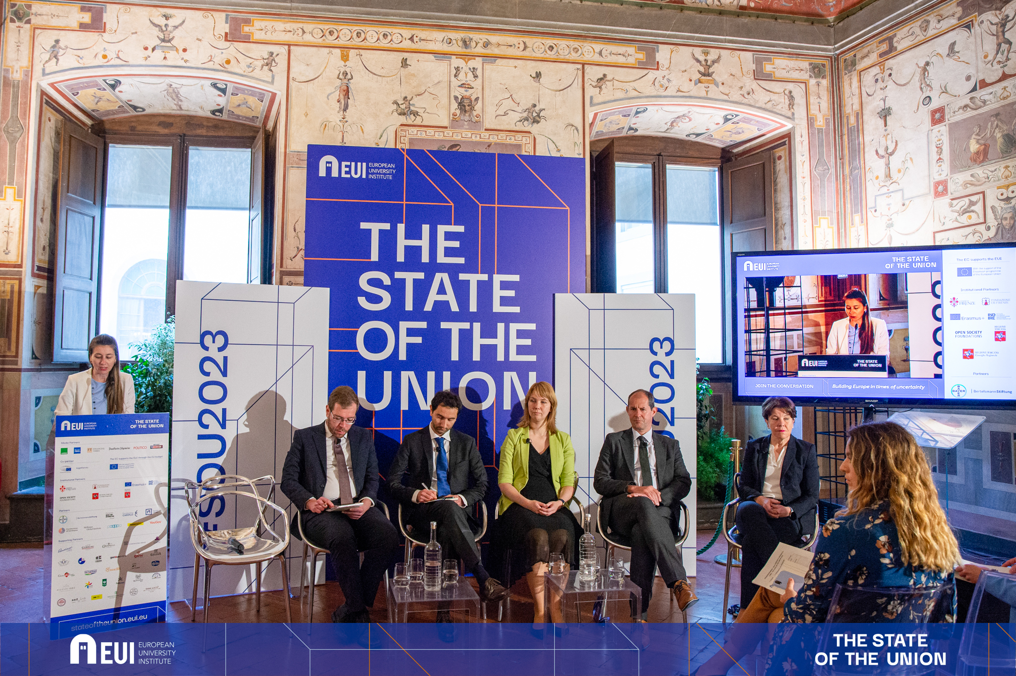 Speaker at podium and panellists sitting on chairs in front of banners with the name of the conference © EUI