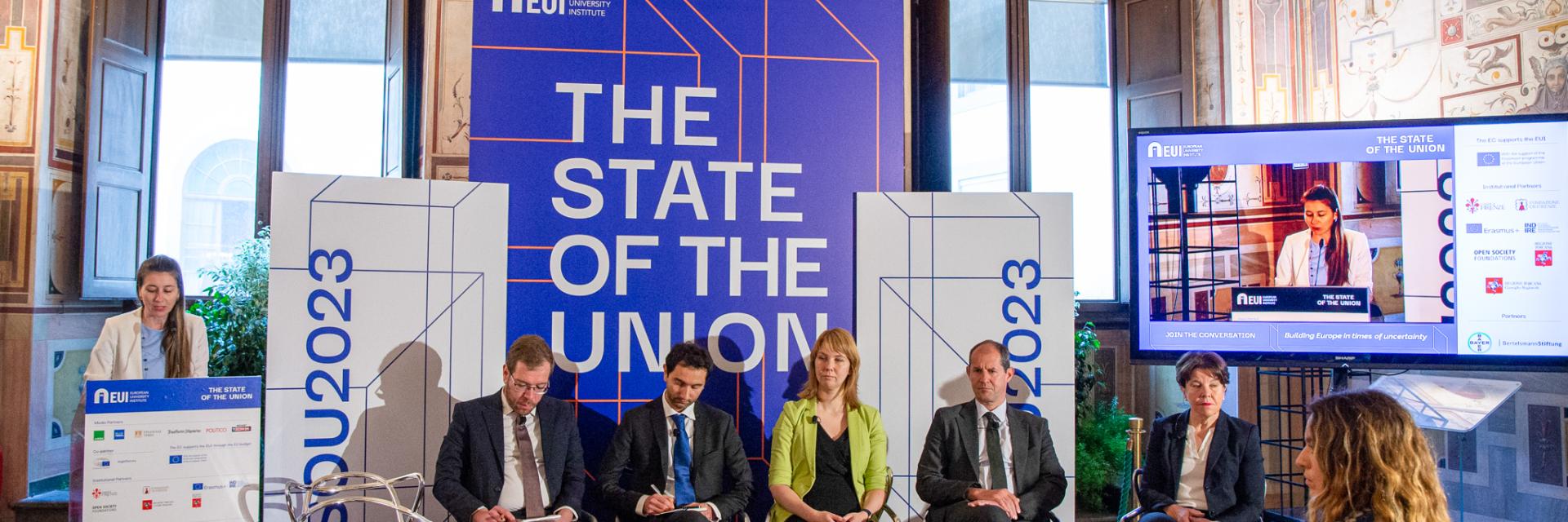 Speaker at podium and panellists sitting on chairs in front of banners with the name of the conference © EUI