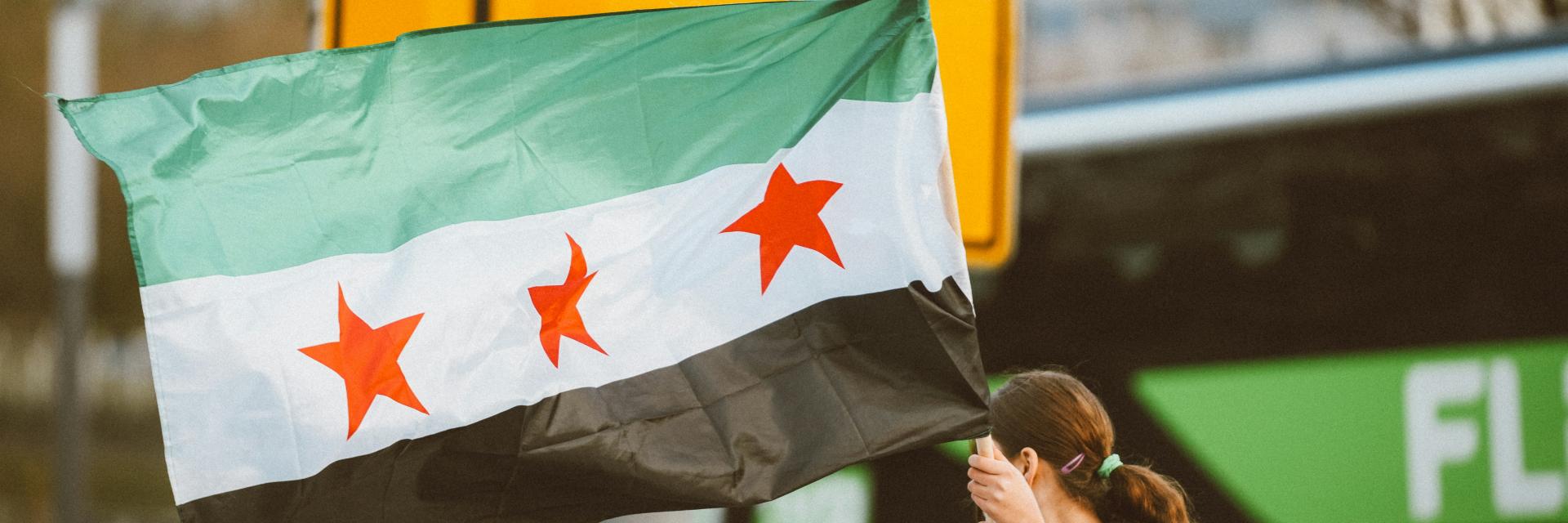 A woman holding the Syrian flag on top of a car | © Omar Ramadan, Unsplash