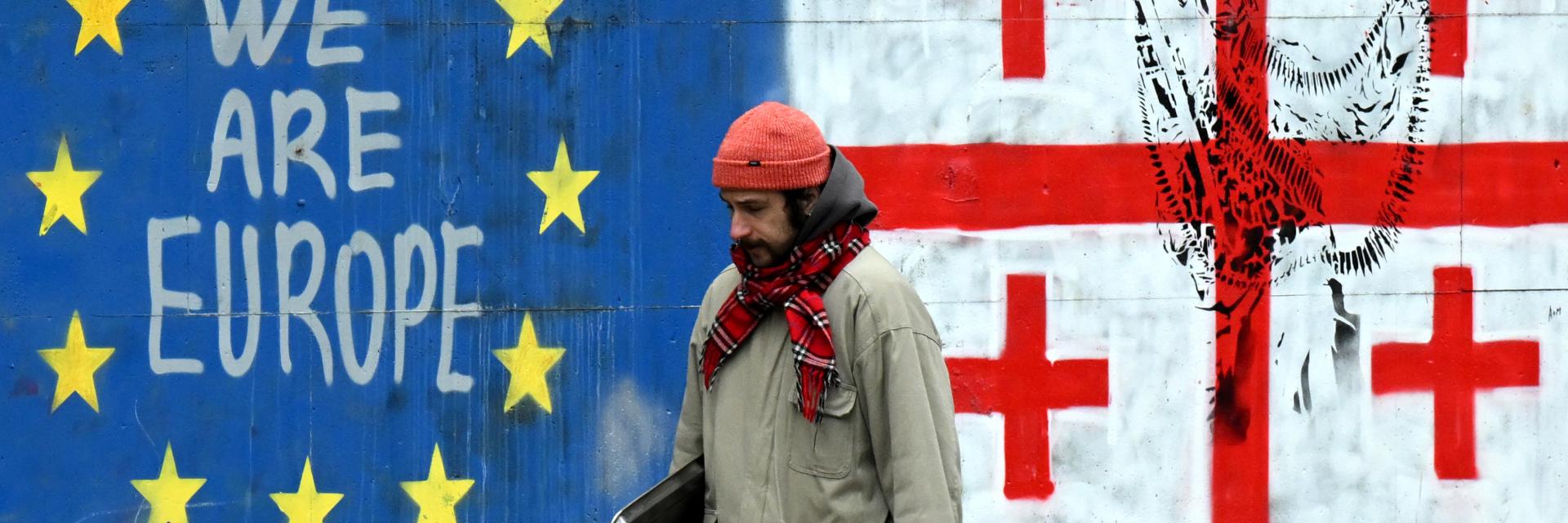 A man walking down a street adorned with graffiti featuring the flags of the European Union and Georgia | © European Union, 2025
