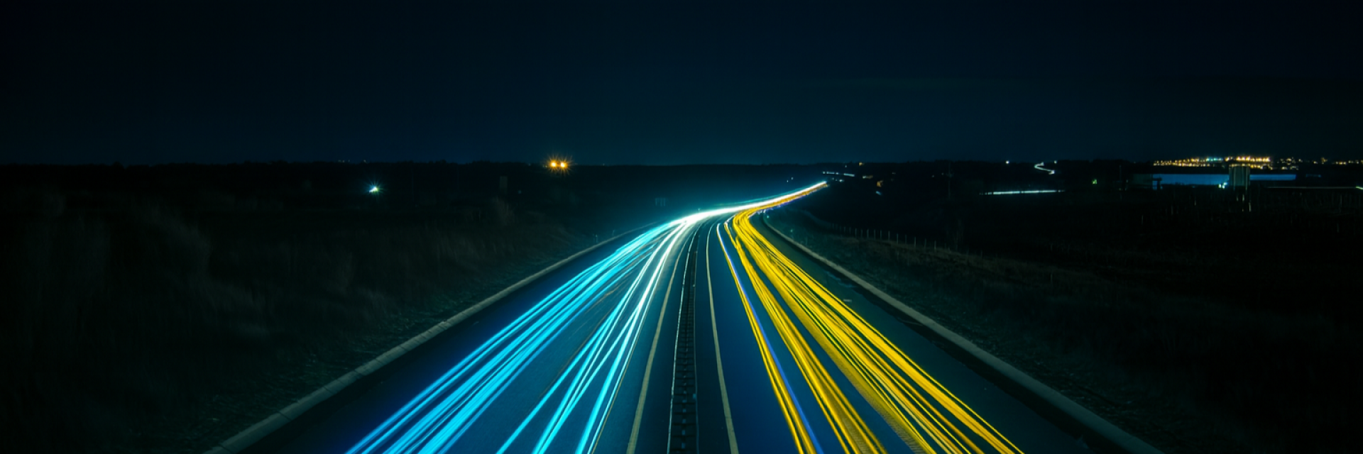 Night-time motorway with long-exposure light trails in EU blue and yellow, converging toward the horizon. Photo by Florian Steciuk on Unsplash (colour edited)