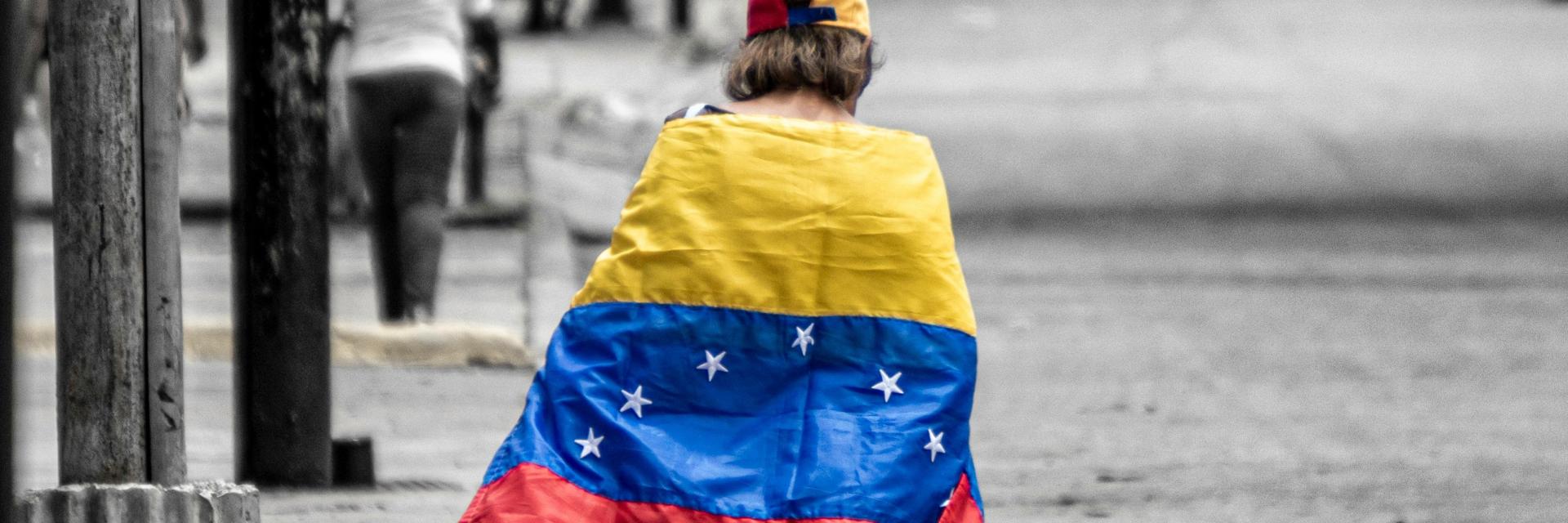 Boy walking in the street with a Venezuelan flag draped over his shoulders. Photo by Andrés Silva on Unsplash 