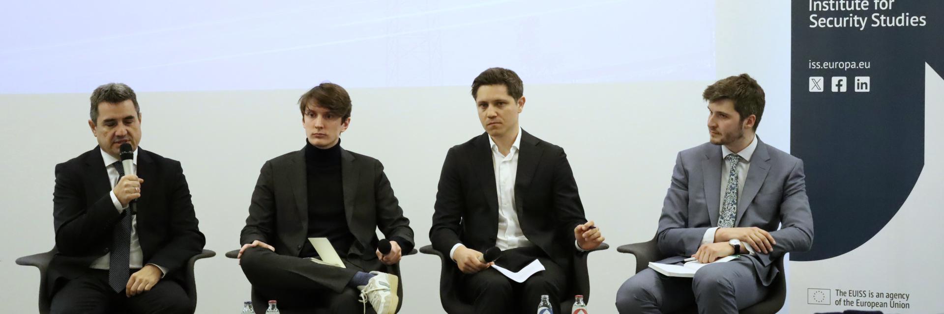 Four men sitting in front of a screen with the name of the event next to EUISS banner. One man is speaking in a microphone. Credit photo: EUISS