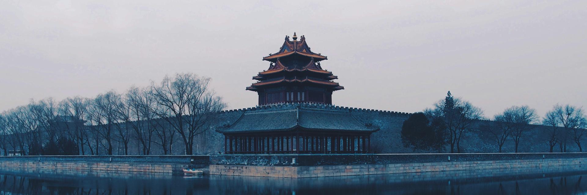 Misty view of a traditional Chinese watchtower beside water, reflected in the surface. Credit photo:Rita Chou/Unsplash