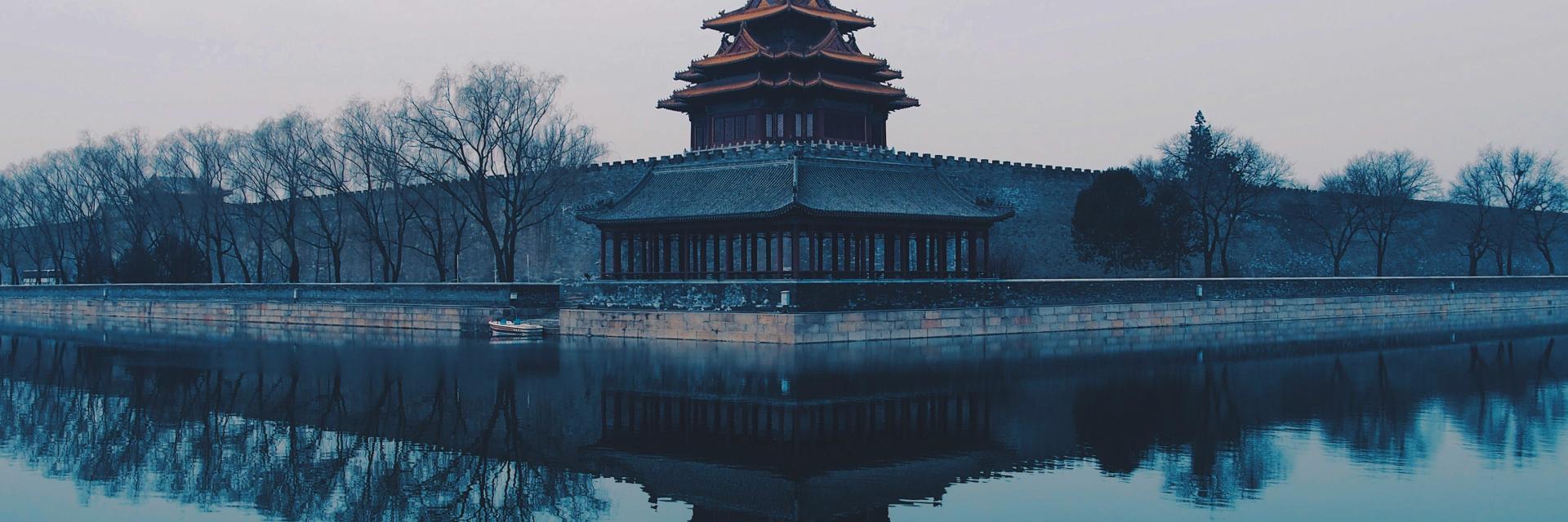 Misty view of a traditional Chinese watchtower beside water, reflected in the surface. Credit photo:Rita Chou/Unsplash