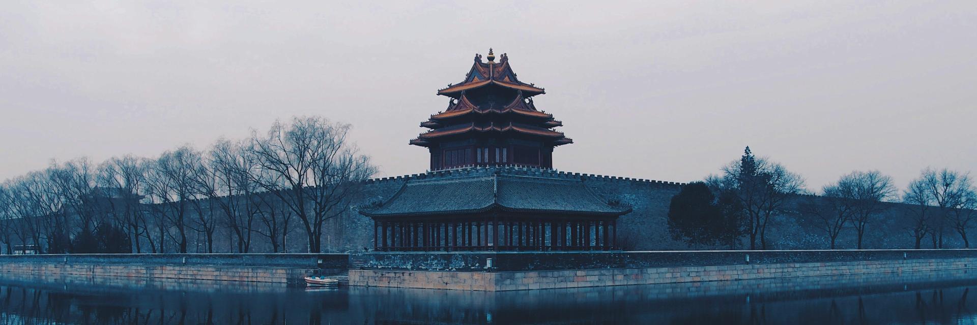 Misty view of a traditional Chinese watchtower beside water, reflected in the surface. Credit photo:Rita Chou/Unsplash