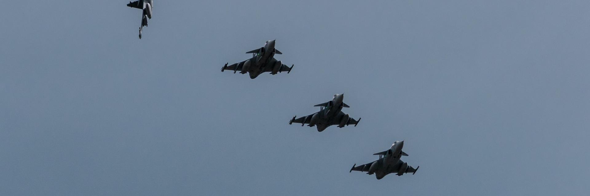 Four military jets are flying in formation against a clear blue sky. Image credit to NATO on Flickr.