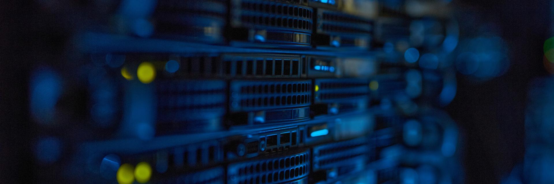 Rows of server racks with blue lighting and small yellow indicator lights in a dark data center environment. Image credit to Envato Elements.