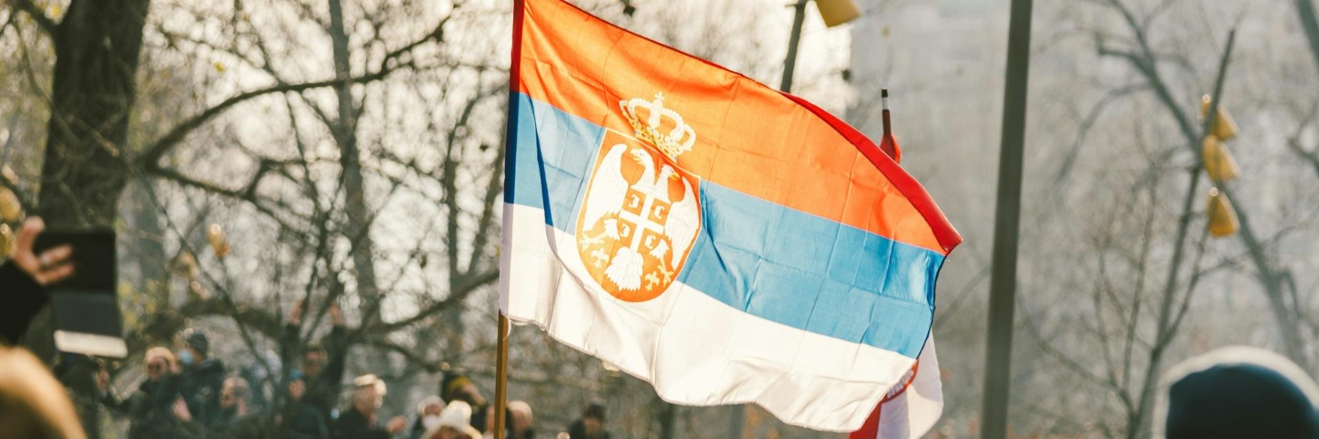 A crowd of people standing around a Serbian flag. Image credit to Stefan Kostic on Unsplash.