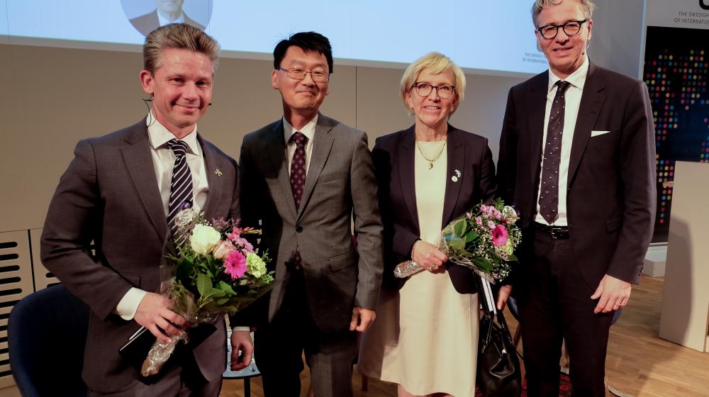 Panelists (three men and one women) posing for photo with bouquet of flowers © UI