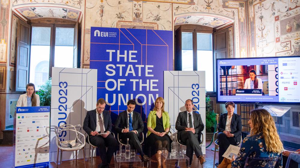 Speaker at podium and panellists sitting on chairs in front of banners with the name of the conference © EUI