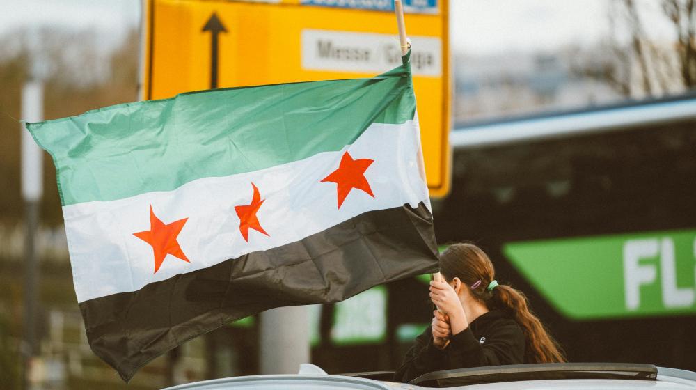A woman holding the Syrian flag on top of a car | © Omar Ramadan, Unsplash