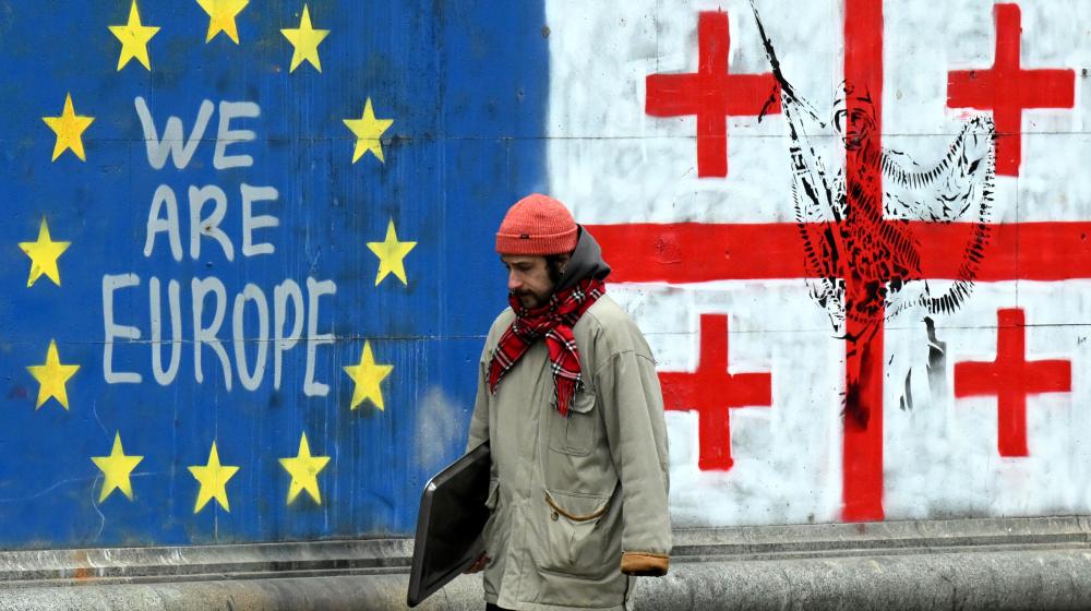 A man walking down a street adorned with graffiti featuring the flags of the European Union and Georgia | © European Union, 2025