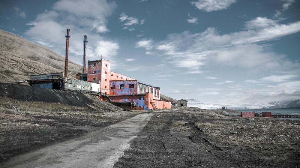 Abandoned industrial buildings of Pyramiden on Svalbard stand weathered and colorful against a stark Arctic landscape and glacier backdrop.
