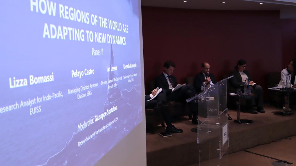 Speakers sitting on stage and title of the session on a screen next to them. Credit photo: EUISS