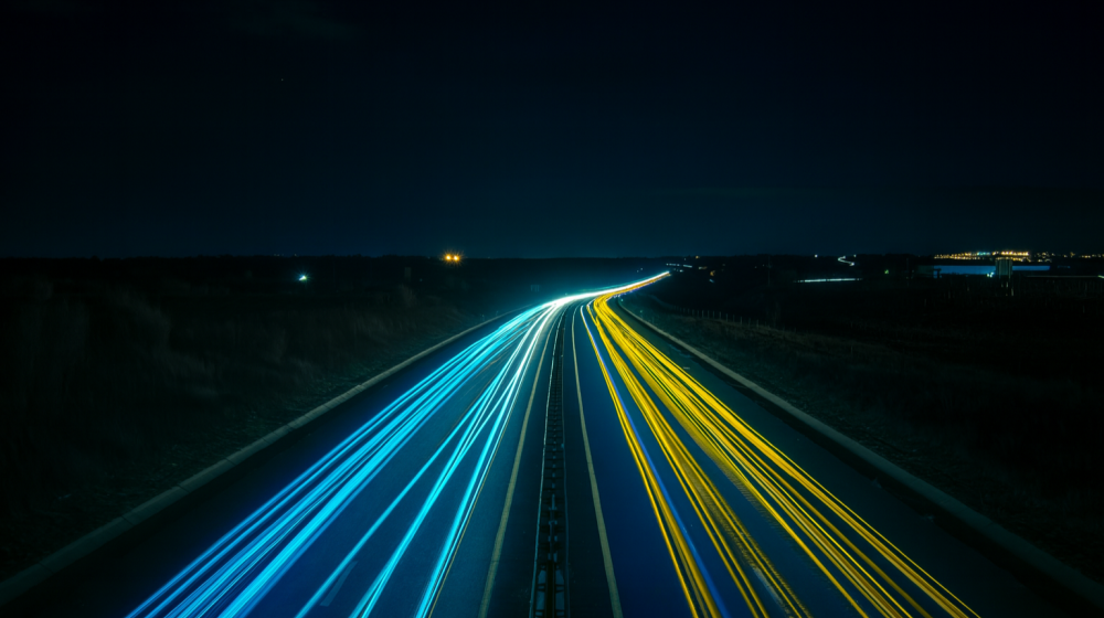 Night-time motorway with long-exposure light trails in EU blue and yellow, converging toward the horizon. Photo by Florian Steciuk on Unsplash (colour edited)