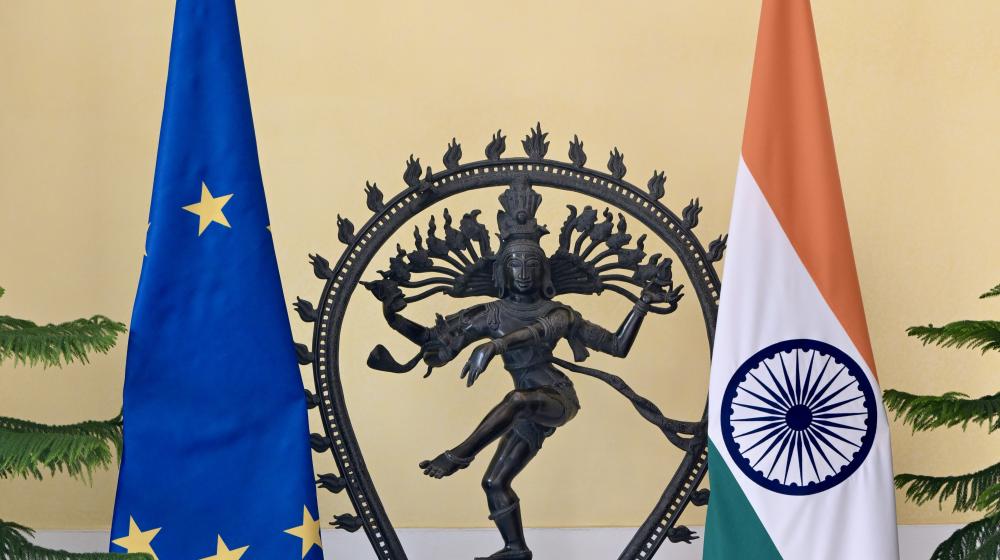 A statue of Shiva as Nataraja stands between the European Union flag and the Indian national flag indoors. Image credit: European Union, 2025