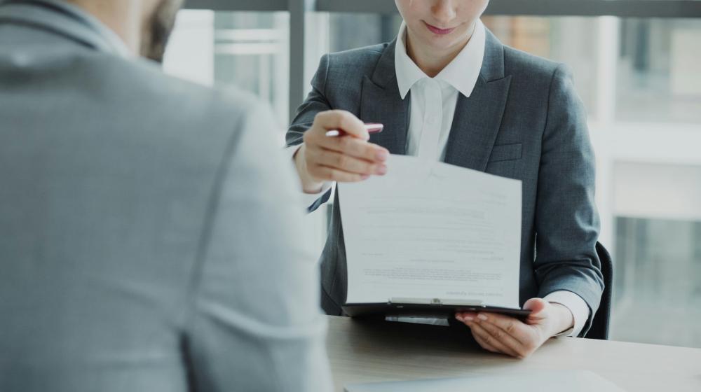 HR businesswoman having job interview with young man in suit and watching his resume application in modern office indoors | © Vitaly Gariev