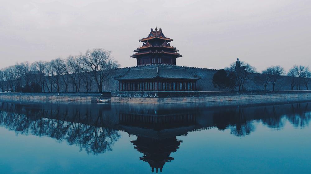 Misty view of a traditional Chinese watchtower beside water, reflected in the surface. Credit photo:Rita Chou/Unsplash