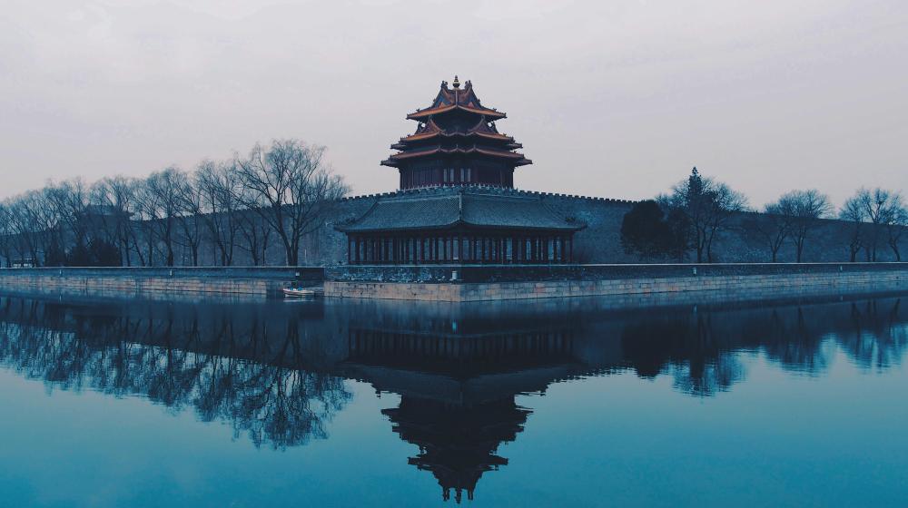 Misty view of a traditional Chinese watchtower beside water, reflected in the surface. Credit photo:Rita Chou/Unsplash