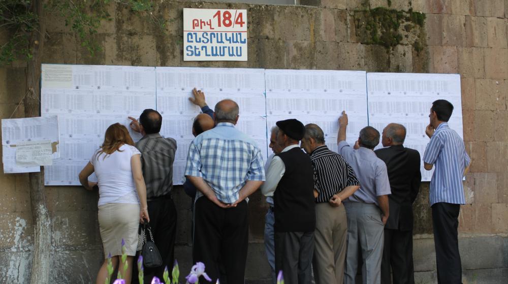 Armenian voters look for their names on voter lists displayed on a wall. Photo by OSCE Parliamentary Assembly, CC BY-NC-SA 2.0