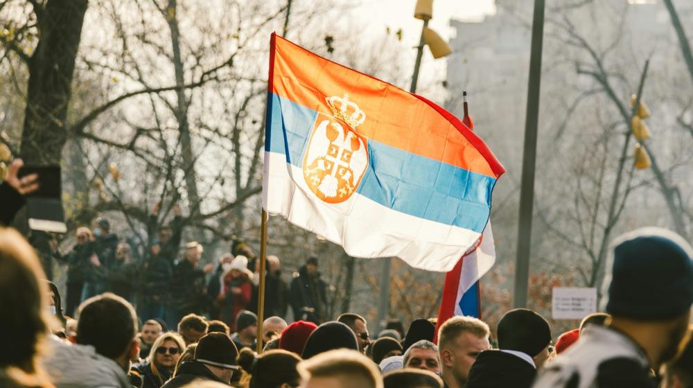 A crowd of people standing around a Serbian flag. Image credit to Stefan Kostic on Unsplash.