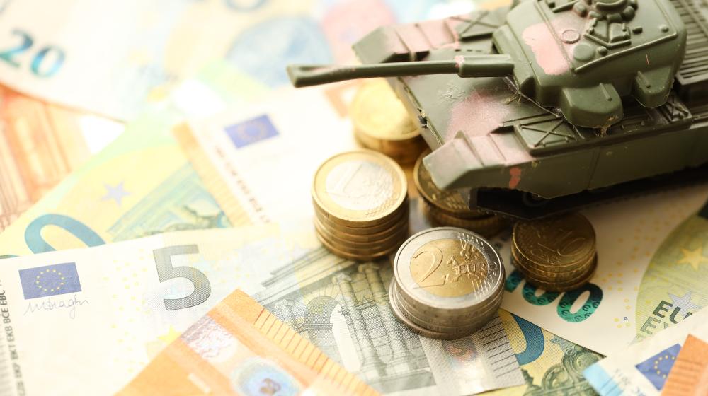 A toy military tank sits atop a pile of Euro notes and coins.