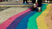 Close-up on the legs of a person wearing sport shoes and walking on a road where a rainbow has been painted on. Photo by Bella The Brave on Unsplash