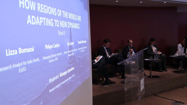 Speakers sitting on stage and title of the session on a screen next to them. Credit photo: EUISS